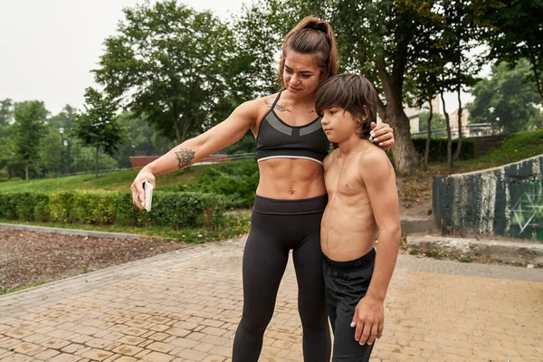 Atletik anne ve oğul akıllı telefondan selfie çekiyorlar.