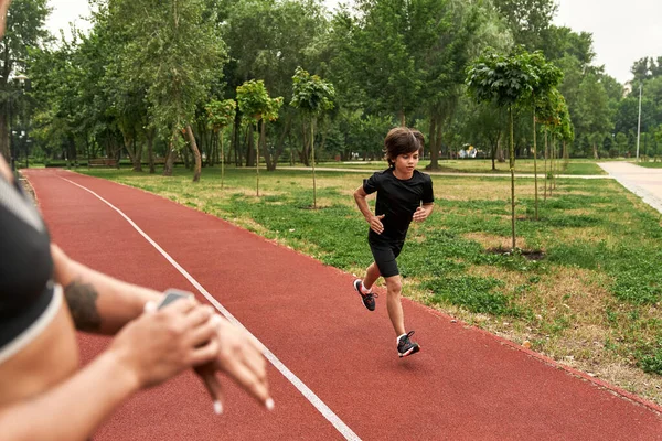 Beskuren tränare notera tid på smartwatch av springa pojke — Stockfoto