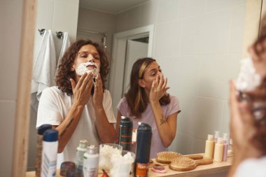 Erkek tıraş köpüğü sürüyor ve kız kremi sürüyor.