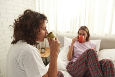 Adam yatakta bulanık bir kızla çay ya da kahve içiyor.