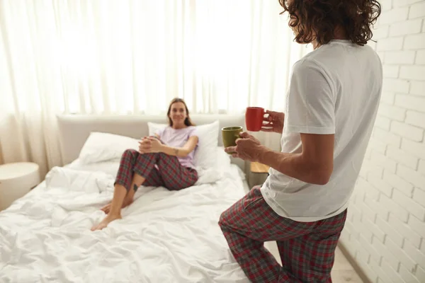 Man carrying tea or coffee to blurred girl on bed — Foto Stock