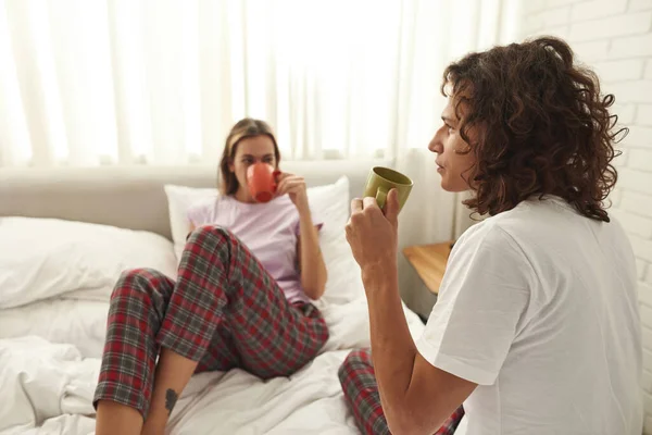 Thoughtful guy drinking tea with girlfriend on bed — Foto Stock
