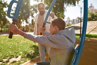 Baba oğlunun spor sahasında egzersiz yapmasına yardım ediyor.
