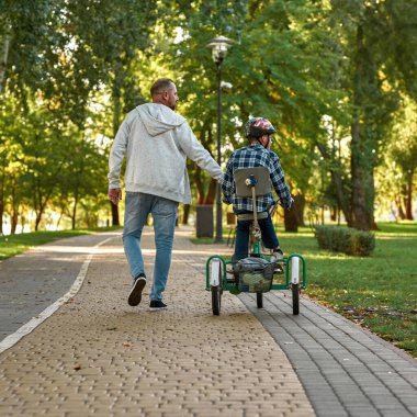 Babanın arkadan görünüşü, oğluyla yürümesi, üç tekerlekli bisiklet.