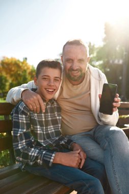 Baba akıllı telefonu göster ve oğlunla kameraya bak.