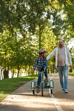 Baba yürü, uzaklara bak ve oğluna üç tekerlekli bisiklet sürmesinde yardım et.