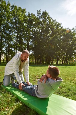 Baba, özürlü oğluna çimenlikte yardım eder.