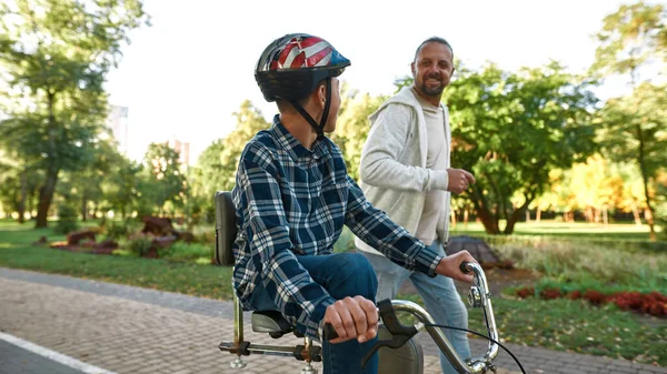 Μπαμπά τζόκινγκ και χαρούμενος γιος με αναπηρικό ποδήλατο βόλτα — Φωτογραφία Αρχείου