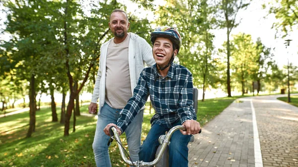 Father jogging while teenage son riding bicycle — Stok fotoğraf