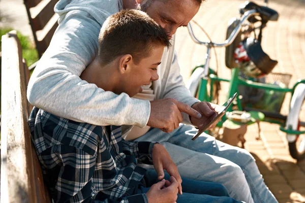 Father and son watch digital tablet in sunny park — Stockfoto