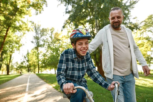 Father walk while joyful teenage son ride bicycle — Stok fotoğraf