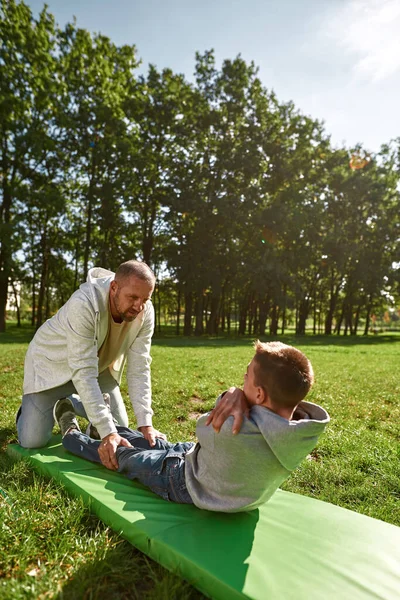 Baba, özürlü oğluna çimenlikte yardım eder.