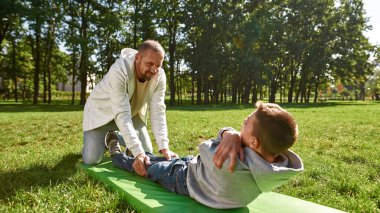 Baba, genç oğlanın parkta spor paspası çiğnemesine yardım et.