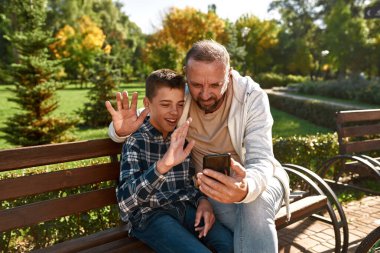 Baba ve oğlanın akıllı telefondan bankta görüntülü görüşmesi var.