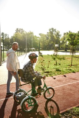 Baba yürü ve üç tekerlekli bisiklete binen genç çocuğa bak.