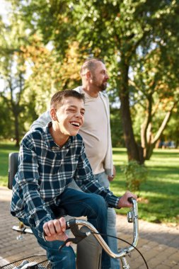 Baba git ve oğluna bisiklete binmesinde yardım et.