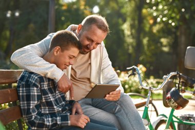 Baba oğul parkta dijital tablet izliyorlar.