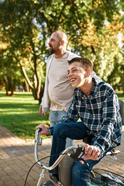 Avrupalı baba yürür ve oğlunun bisiklete binmesine yardım eder
