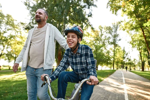 Otec jít zatímco šťastný dospívající syn jízda na kole — Stock fotografie