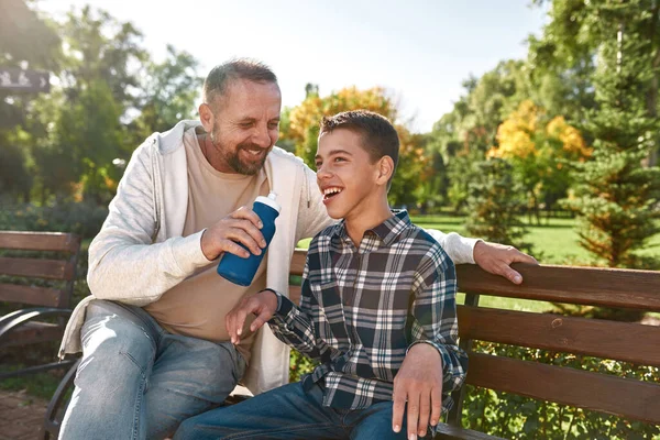 Pai dá água de bebida de garrafa filho adolescente — Fotografia de Stock