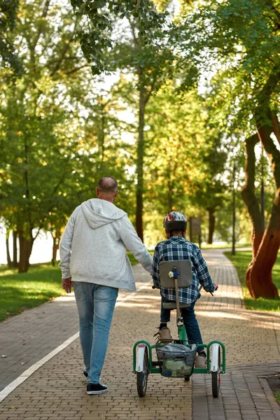 Back of dad help son with handicap ride tricycle — Stock fotografie