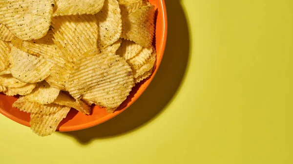 Sarı arka planda patates cipsli kase.