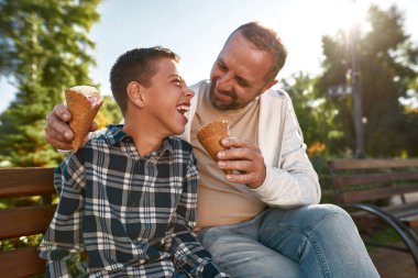 Pleased father feed ice cream and look at son
