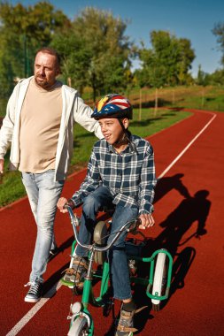 Baba git ve üç tekerlekli bisiklete binmesine yardım et.