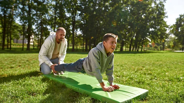 Dad help son with cerebral palsy do plank on lawn — Zdjęcie stockowe