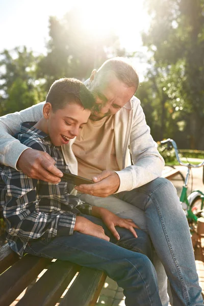 Focused and smiling dad and son watch smartphone — Stok fotoğraf