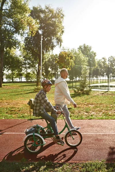 Side view of father walk near son ride tricycle — Foto de Stock