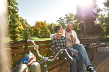 Özürlü baba oğul parkta dondurma yiyorlar.