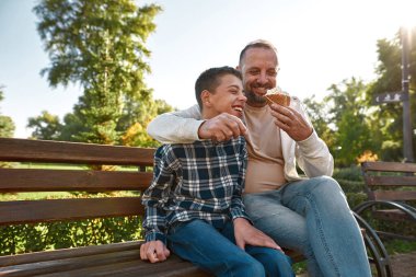 Joyful father and teenage son eat sweet ice cream