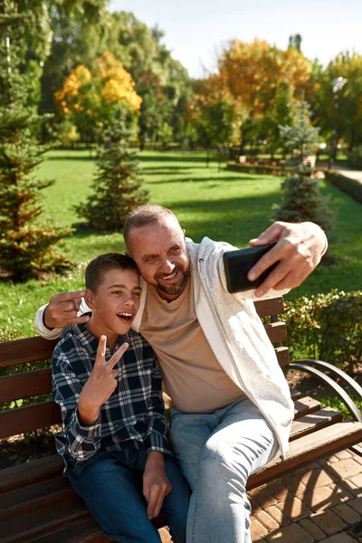 Father and boy taking selfie on smartphone in park — Zdjęcie stockowe