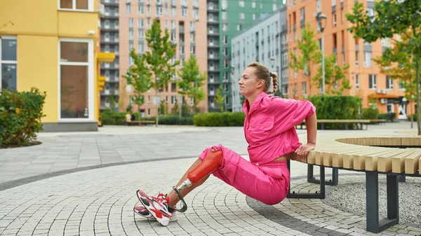 Girl with artificial leg doing exercise on bench
