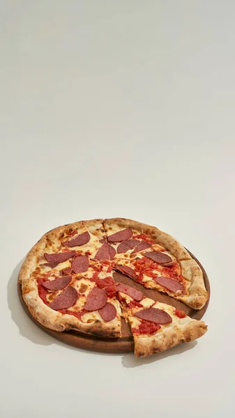 Pizza de pepperoni con una rebanada cortada en el tablero circular — Foto de Stock
