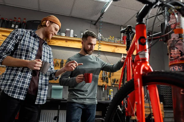 Repairmen checking bicycle and talking in workshop