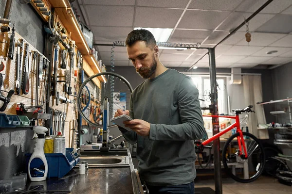 Cycling mechanic writing notes in notebook at work
