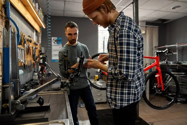 Hombre con cuaderno cerca de chico que mide horquilla de bicicleta — Foto de Stock