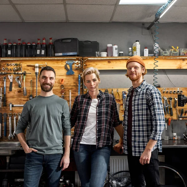 Drei selbstbewusste Radmeister in Fahrradwerkstatt — Stockfoto