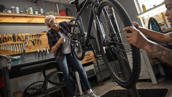 女の子のマスターは、ワークショップで自転車にホイールをインストールします — ストック写真