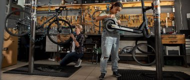 Afrika kökenli Amerikalı bir zanaatkar modern atölyeye ingiliz anahtarı takan beyaz kadın meslektaşının yanında elektrikli scooter 'ı tamir ediyor. Bisiklet servisi, tamir ve geliştirme