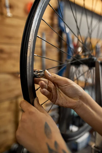 自転車の車輪をチェックする女性の自転車整備士の手の作物のイメージは ブルーモダンのワークショップでレンチを話しました タトゥーのある黒人女性 自転車サービス 修理とアップグレード — ストック写真