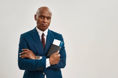Ciddi bir zenci işadamı uçak biletleriyle cüzdan tutuyor. Yetişkin bir adam resmi giyinmiş ve kameraya bakıyor. Modern başarılı erkek yaşam tarzı. Beyaz arka plan. Stüdyo çekimi. Boşluğu kopyala