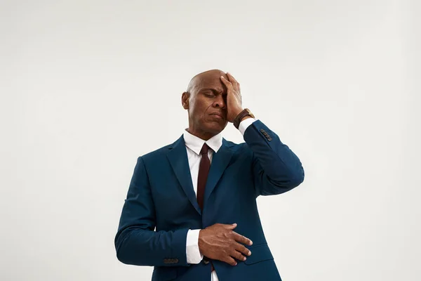 Tired black entrepreneur with migraine touching his head. Bald adult man wearing formal wear. Concept of modern successful male lifestyle. Isolated on white background. Studio shoot. Copy space