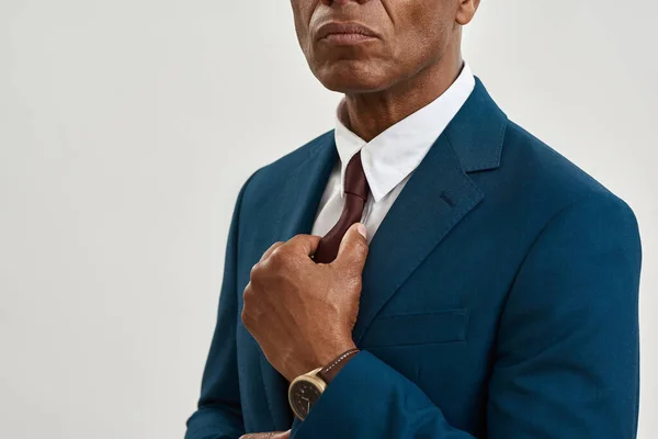 Cropped image and obscure face of serious adult black entrepreneur straighten tie of his formal wear. Modern successful male lifestyle. Isolated on white background. Studio shoot. Copy space