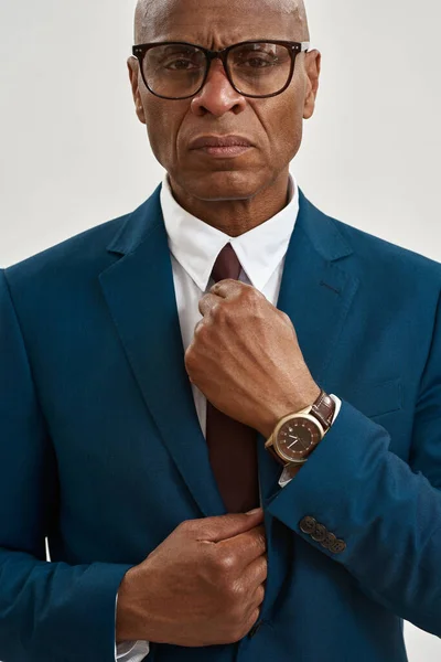Cropped image and obscure face of serious adult african american company leader wear glasses straighten tie of his suit. Modern successful male lifestyle. Isolated on white background. Studio shoot