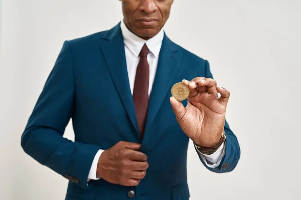 Obscure face of black financial investor holding crypto coin. Man wearing formal wear. Modern successful male lifestyle. Cryptocurrency for digital payment. White background. Studio shoot. Copy space