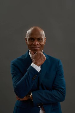 Kameraya gülümseyen Afro-Amerikan iş adamının ön görüntüsü. Takım elbiseli kel bir yetişkin. Modern başarılı erkek yaşam tarzı kavramı. Gri arka planda izole edilmiş. Stüdyo çekimi. Boşluğu kopyala