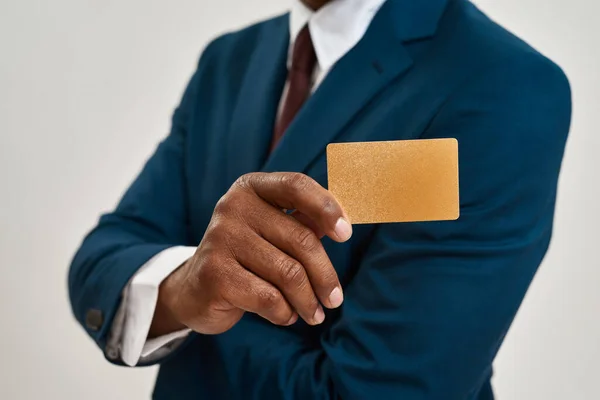 Selective focus of golden business card in hand of blurred african american ceo manager or entrepreneur. Man wearing suit. Concept of modern successful male lifestyle. White background. Studio shoot